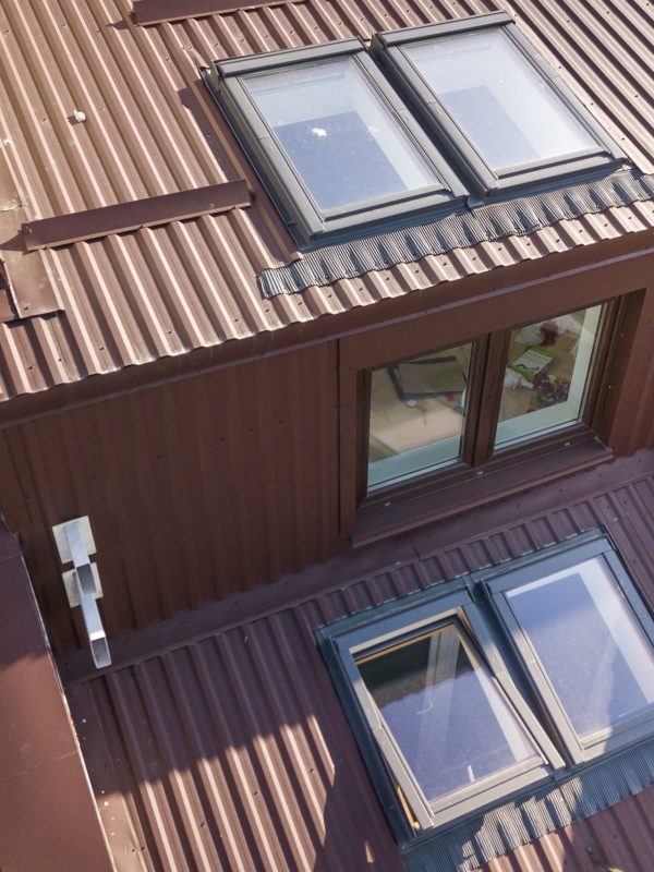Aerial view of annex room exterior with plastic attic windows, roof and walls covered with brown metal decorative siding planks.